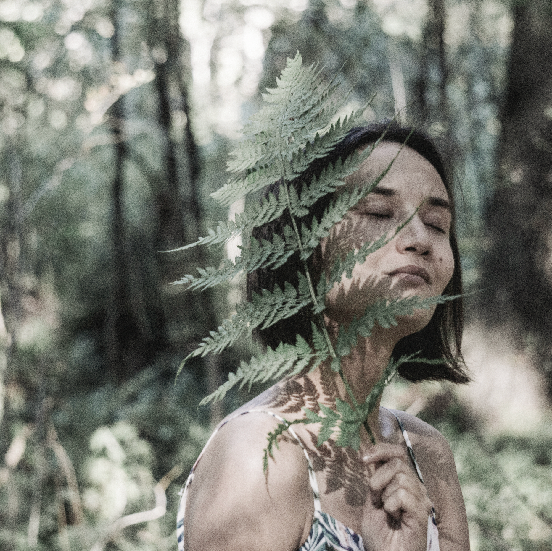Woman holding fern leaf with eyes closed in peaceful forest setting representing ABENDHAUCH fragrance with eucalyptus, mint, and sandalwood notes